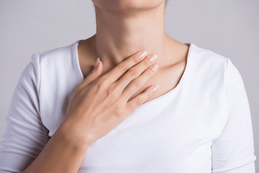 A woman placing her hand over her thyroid.